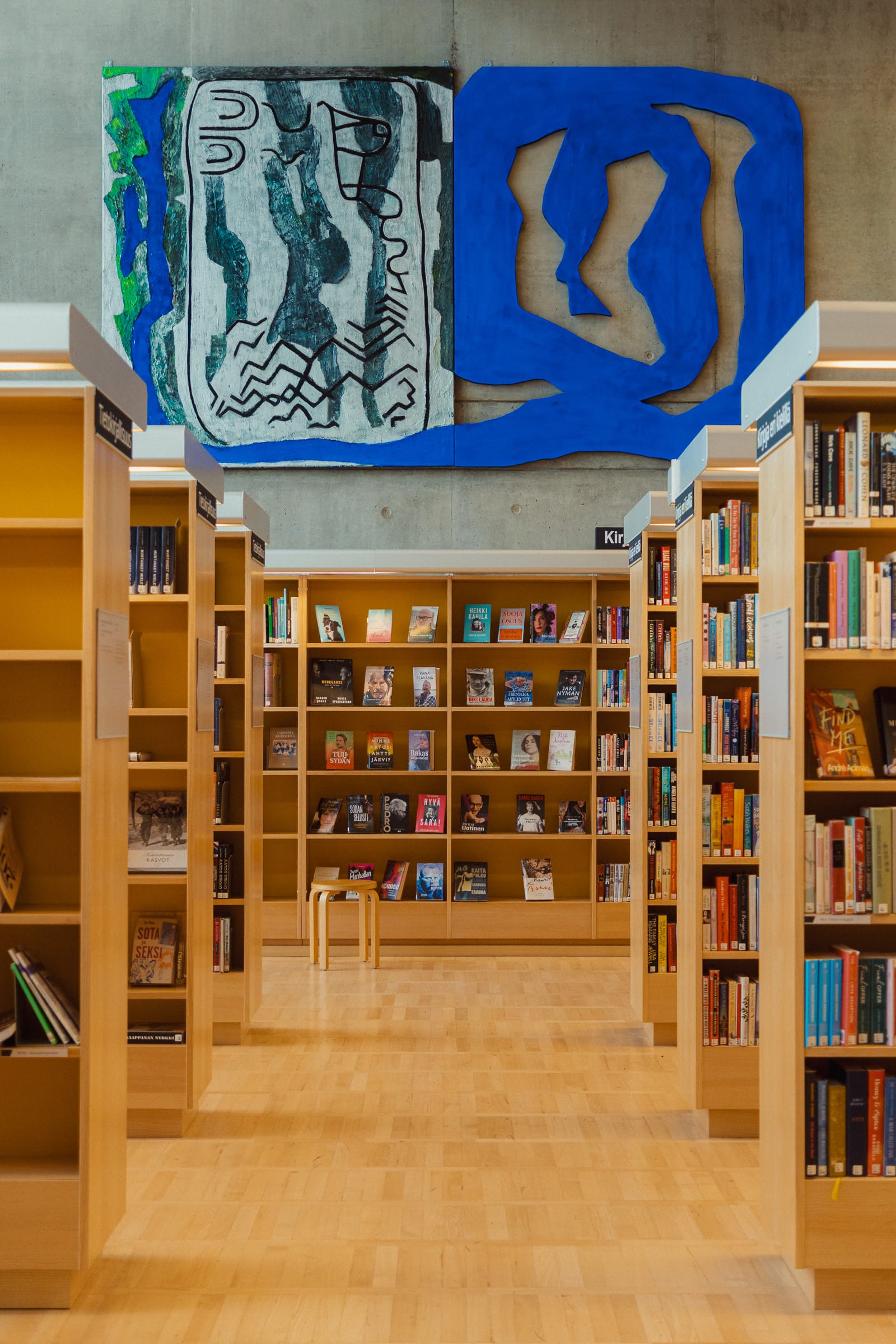 Bücherregal aus Holz, darüber ein Kunstwerk auf Betonwand